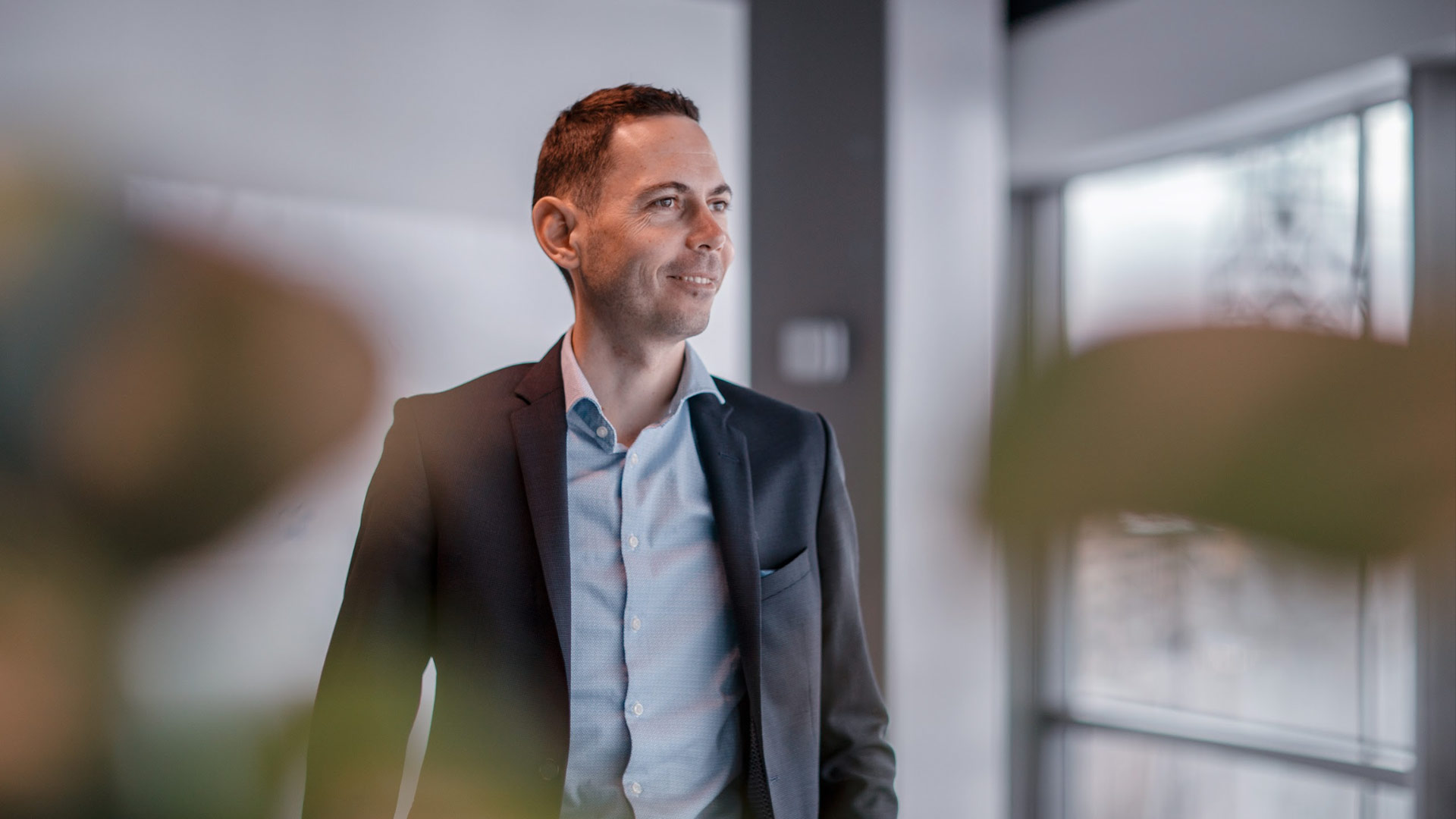 A smiling Gregory Bolard stands in an office, slightly turned away from the camera.